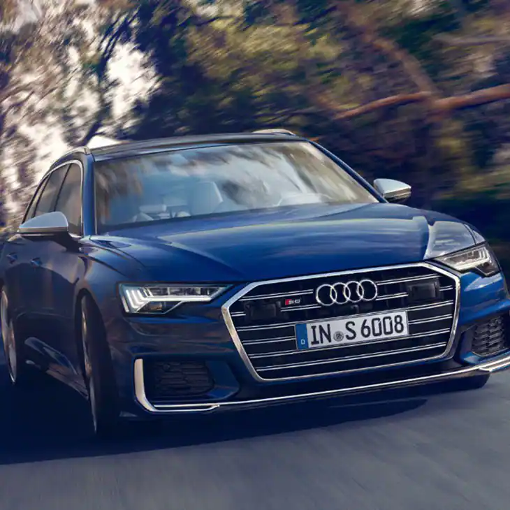front view of a blue audi s6 avant driving with trees on either side