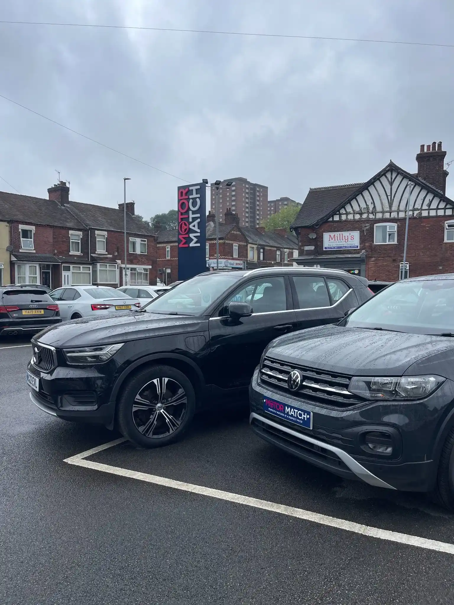 cars parked outside of a motor match dealership with a sign in the background