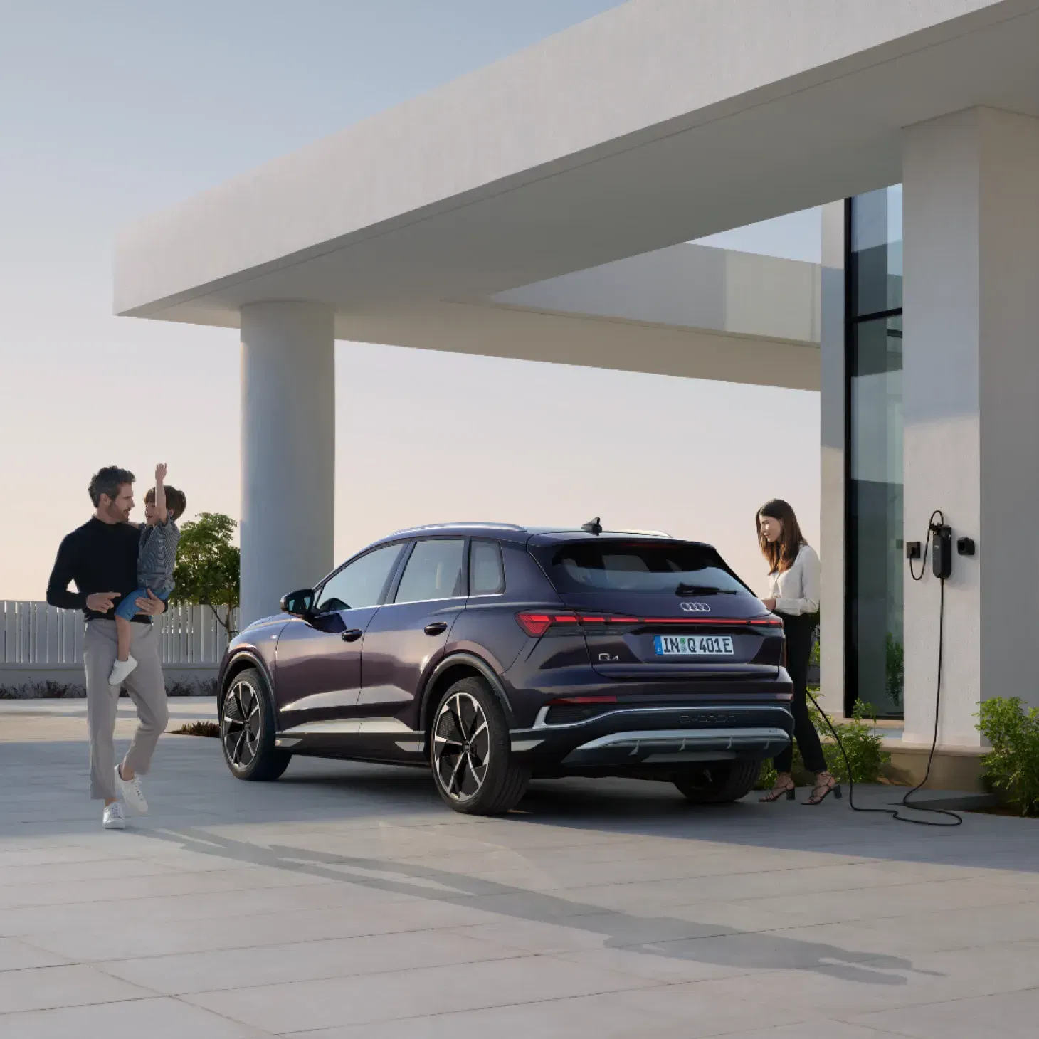 Woman charging an Audi Q4 outside a house with a man carrying a child
